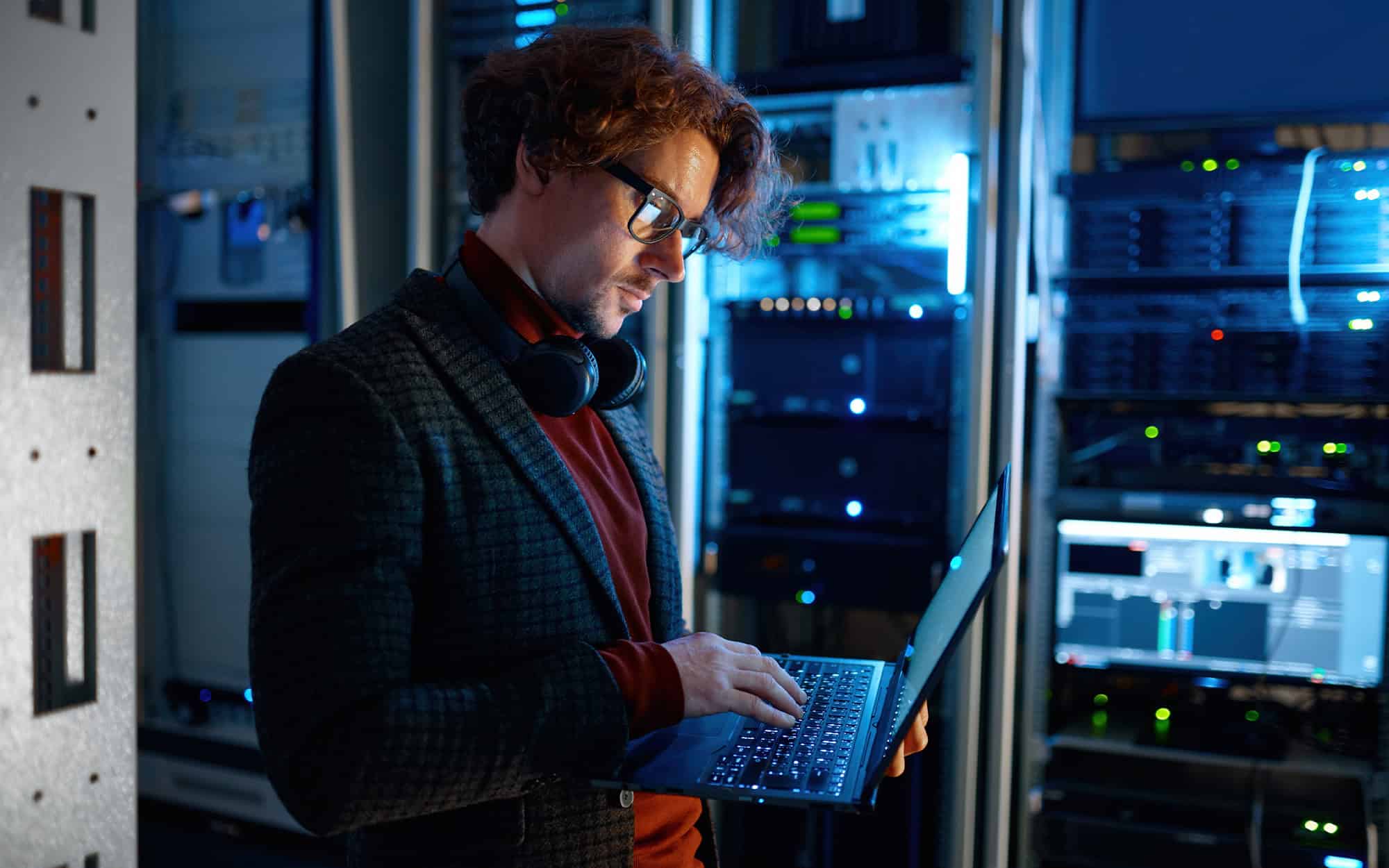 Side View Of Man Working On Laptop Standing In Server Room