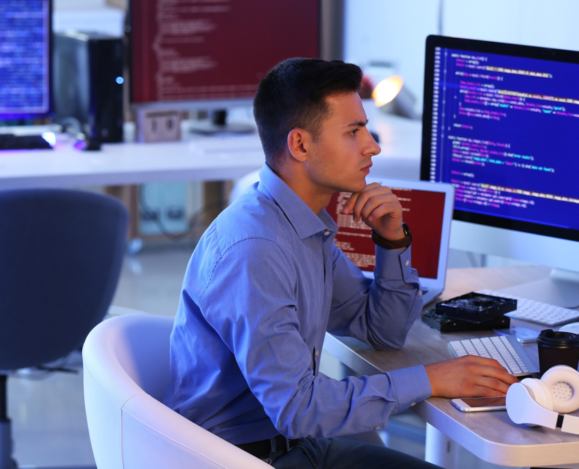 Side View Of Young Cybersecurity Professional Looking At Multiple Monitors